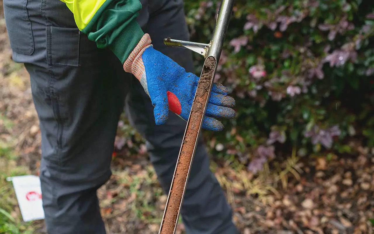 A gloved hand taking a soil sample with a probe
